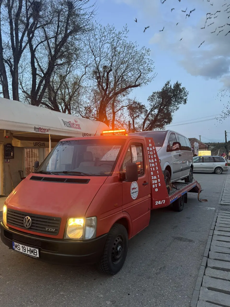 Platforma cu girofarul pornit, la apus, cu o mașină albă pe ea