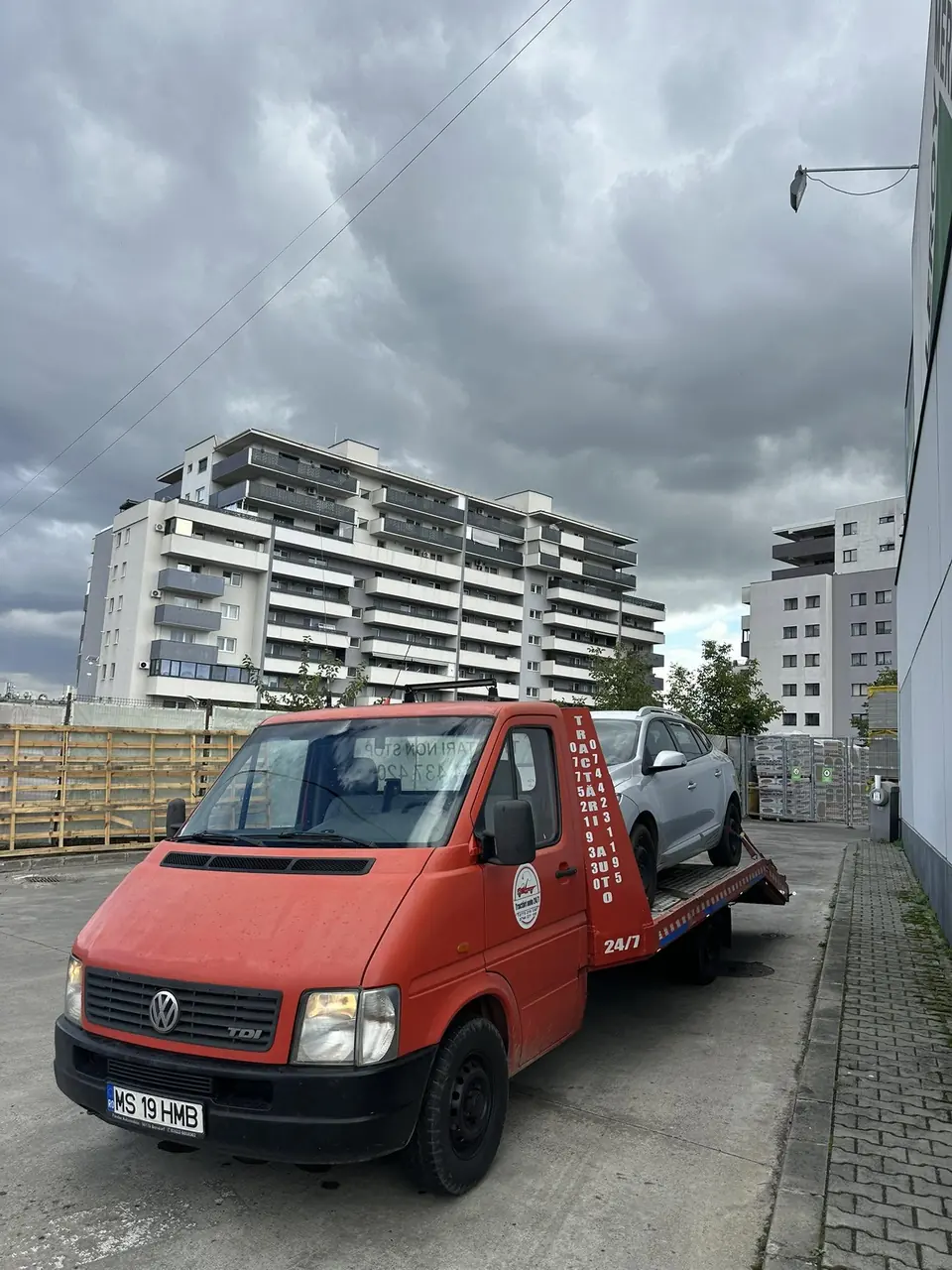 Mașină livrată cu platforma în fața unui bloc nou